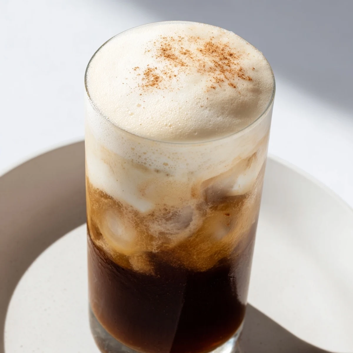 Iced Chai Tea with Cold Foam served in a clear glass over ice, with a light dusting of cinnamon garnish.  