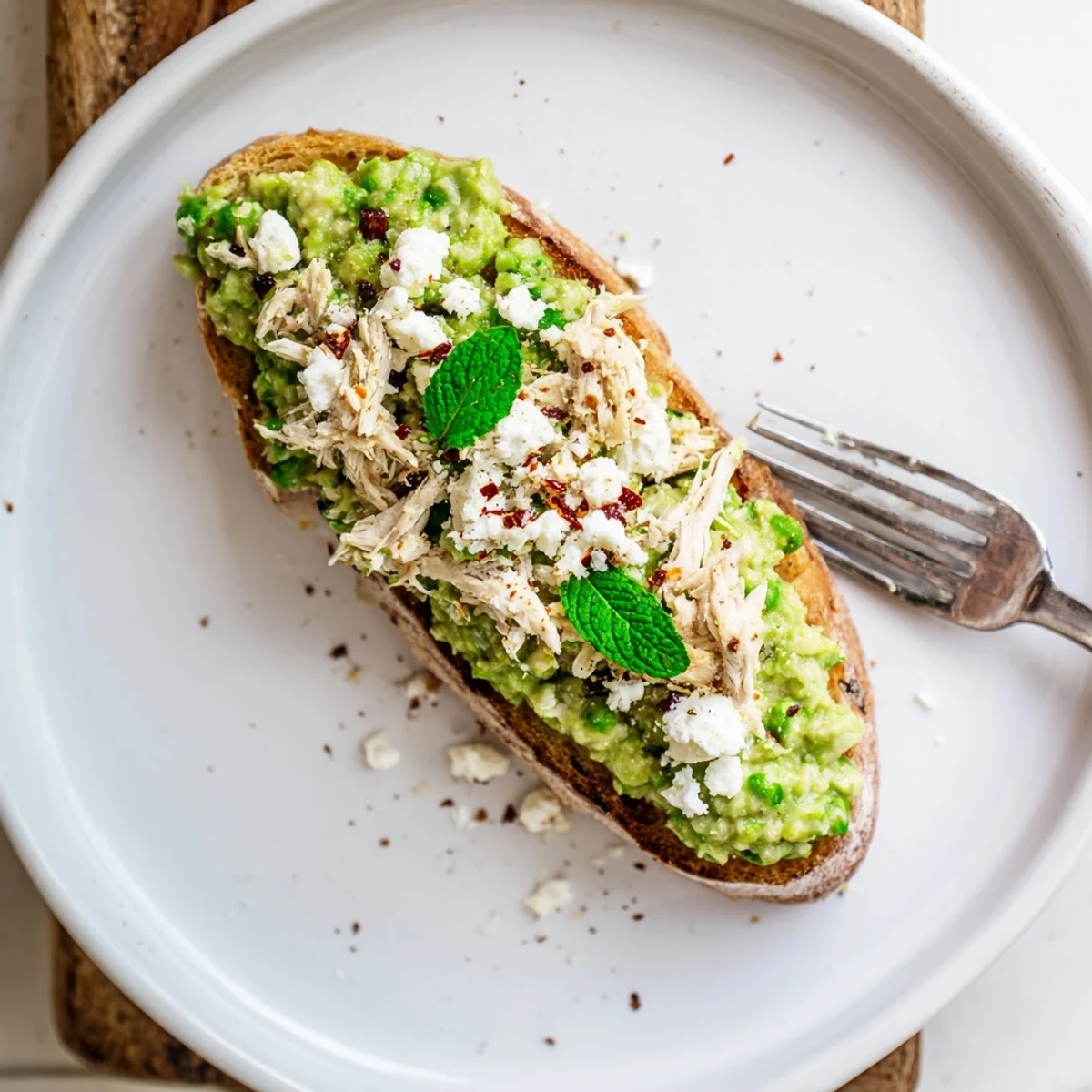 Golden-brown sourdough toast topped with creamy smashed pea and shredded chicken mixture, garnished with chili flakes.