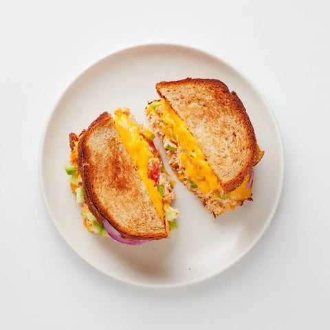 Golden-brown sourdough slices, filled with zesty spicy tuna melt and gooey melted cheddar, served hot on a plate.