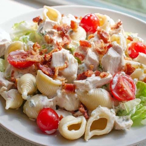 A close-up of BLT Chicken Pasta Salad with grilled chicken, crisp bacon, and halved cherry tomatoes on pasta shells, dressed in creamy mayo.  