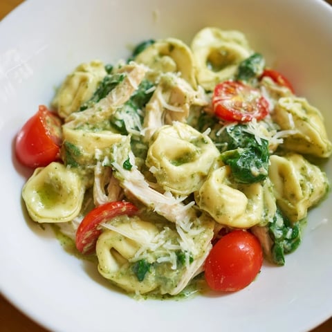 A close-up of creamy pesto tortellini skillet bubbling in a cast iron pan, topped with fresh basil and halved cherry tomatoes.  