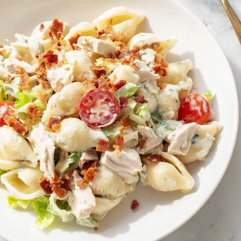 BLT Chicken Pasta Salad served in a white bowl with chopped romaine and red onion, perfect for a hearty summer picnic or lunch.  