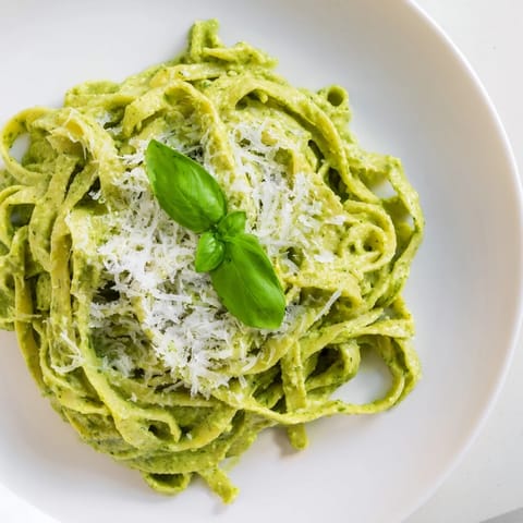 A close-up of green pea Alfredo pasta, with a glossy sauce and herbs, served warm on a plate for a comforting vegetarian meal.
