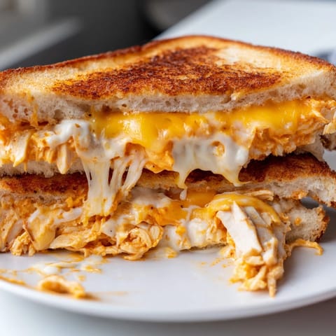 A close-up view of golden-brown bread revealing gooey cheese and buffalo chicken filling for a Buffalo Chicken Ranch Grilled Cheese.  