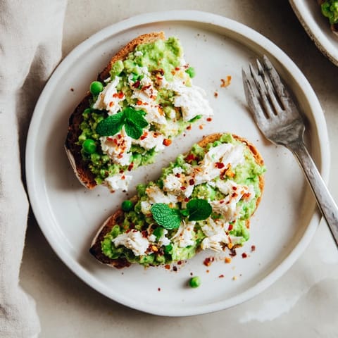 Smashed Pea & Chicken Toast on rustic bread with fresh herbs, ready to serve as a quick lunch.