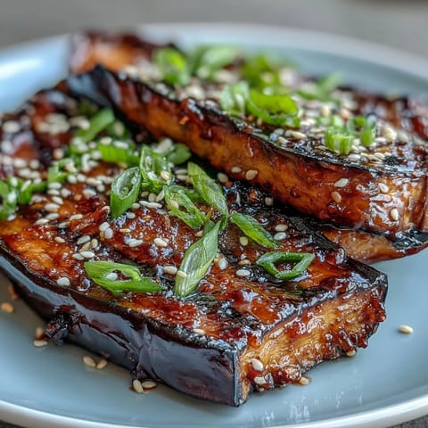 Miso-glazed eggplant steaks with caramelized miso topping and sesame garnish on a white plate.  