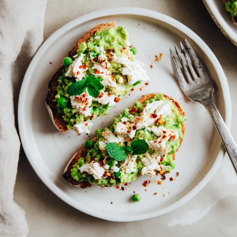 Smashed Pea & Chicken Toast on rustic bread with fresh herbs, ready to serve as a quick lunch.