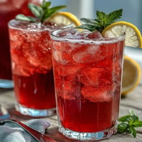 A vibrant glass of sparkling hibiscus mint lemonade mocktail with fresh mint garnish and lemon slices.  